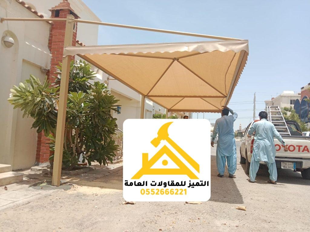 مظلة قماشية كابولية مثبتة على واجهة مبنى فوق مدخل، ويظهر فنيّان أثناء التركيب
