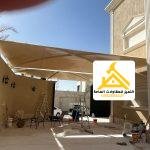 مظلة قماشية بيج مثبتة على جدار المنزل تغطي الفناء