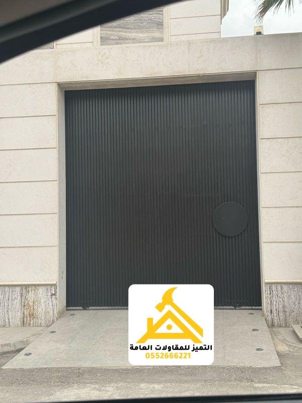 باب حديد عريض بشرائح طولية داكنة في واجهة حجرية