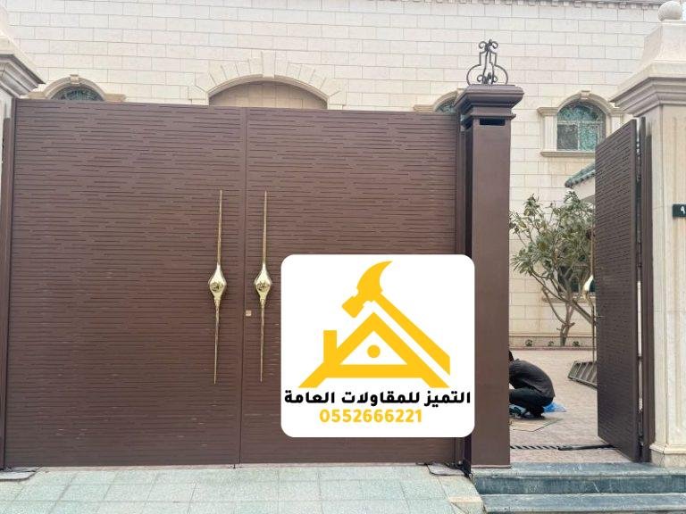 بوابة سيارات حديد بضلفتين بلون بني ومقابض ذهبية بجانب باب مشاة مفتوح