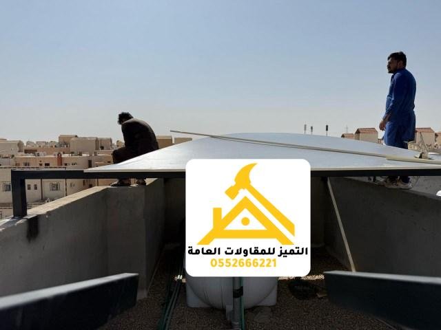 فنيّان يثبّتان مظلة لوحية مسطّحة فوق خزان مياه علوي على سطح مبنى