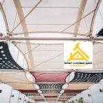 أشرعة قماش بيضاء وأخرى مثقبة تغطي مساحة مفتوحة بارتفاعات متدرجة