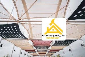 أشرعة قماش بيضاء وأخرى مثقبة تغطي مساحة مفتوحة بارتفاعات متدرجة