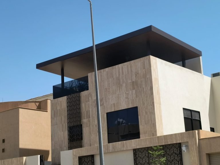 مظلة سطح مسطحة داكنة ممتدة فوق الطابق العلوي لفيلا بواجهة حجرية